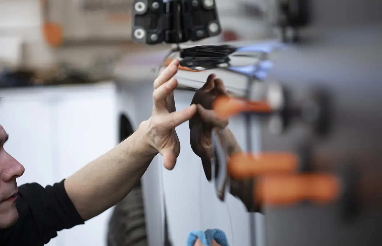 A JLC bodyshop technician running a hand over a freshly finished panel to check the paintwork