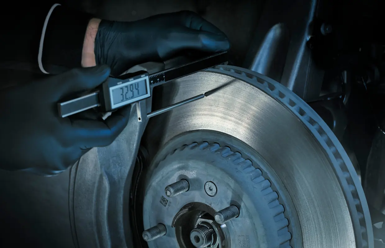 A technician measuring brake disc thickness with a digital gauge during a vehicle health check