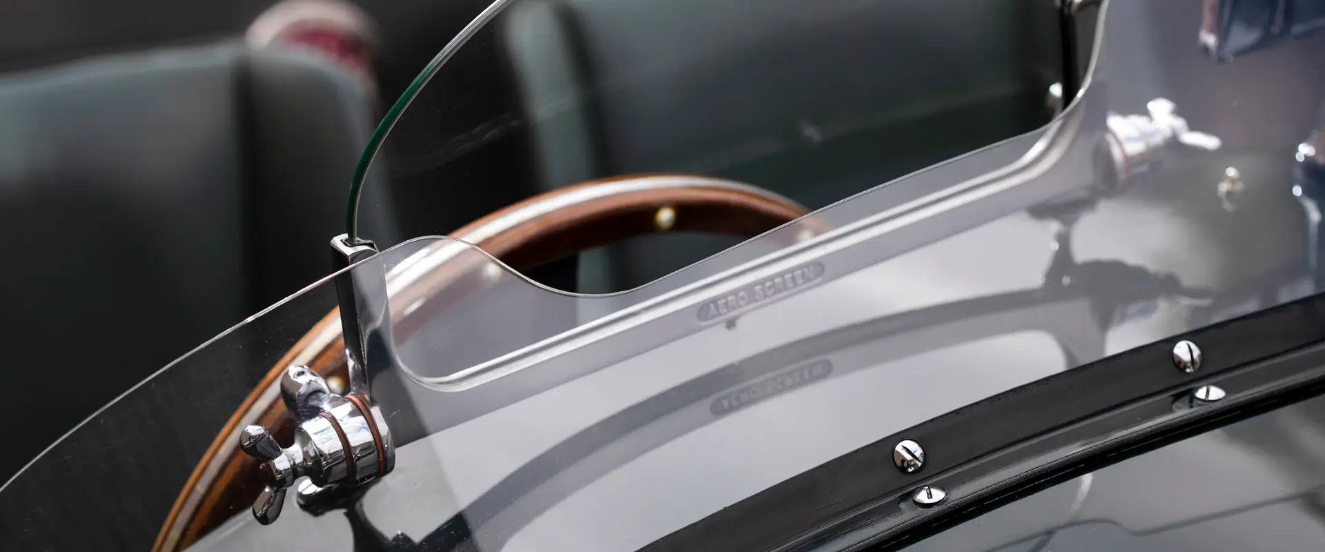 Close-up of the aero screen, wood-rimmed steering wheel and green leather seats of a classic Jaguar