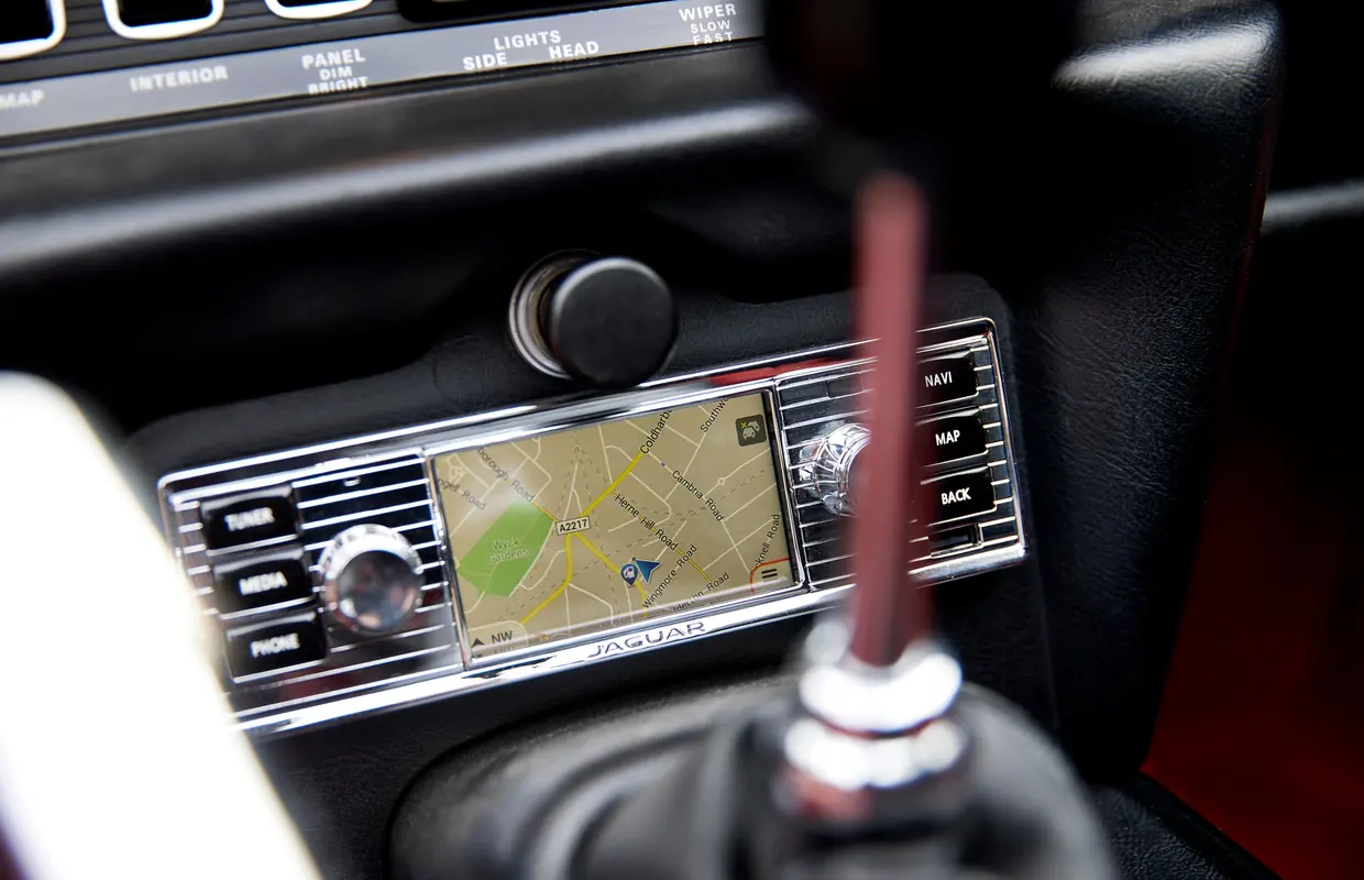 A classic Jaguar dashboard fitted with a period-style radio that houses modern satellite navigation