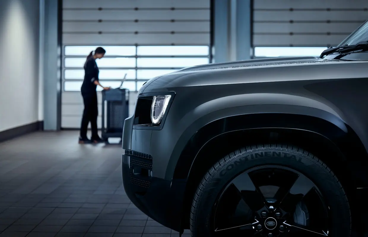 The front of a Land Rover Defender in a service bay with a technician at a workstation behind
