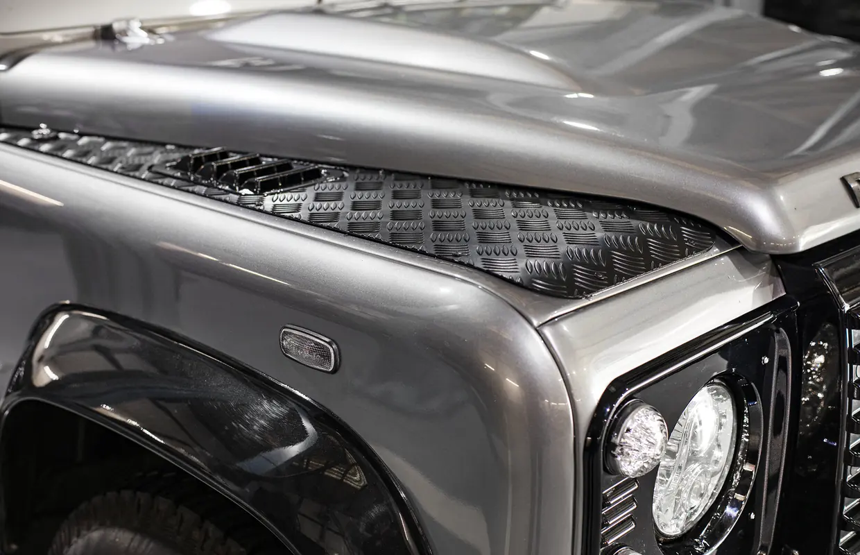 The freshly painted front wing and chequer plate of a grey Land Rover Defender after repair