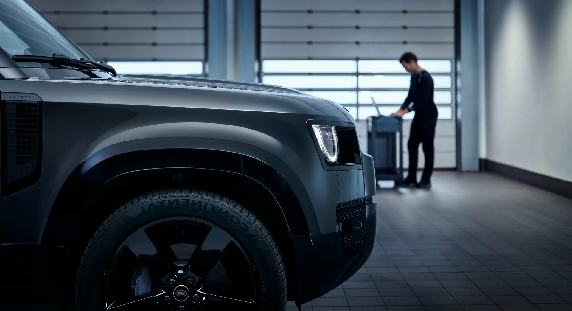 A Land Rover Defender in the JLC workshop with a technician preparing a tool trolley behind it