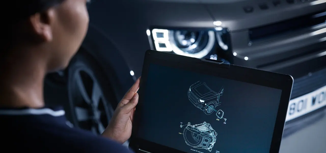 A JLC technician reviewing Jaguar Land Rover diagnostic data on a laptop beside a Defender