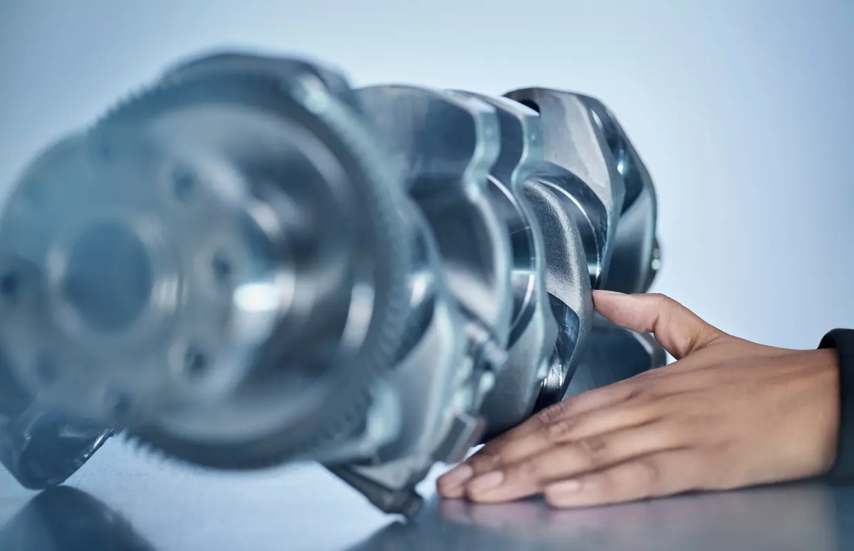 A hand resting on a genuine Jaguar Land Rover crankshaft on the workshop bench