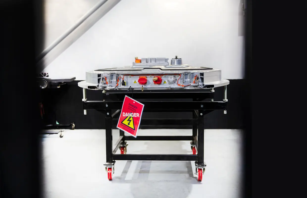 A high-voltage battery pack on a workshop trolley with a Danger, electrical system live warning tag