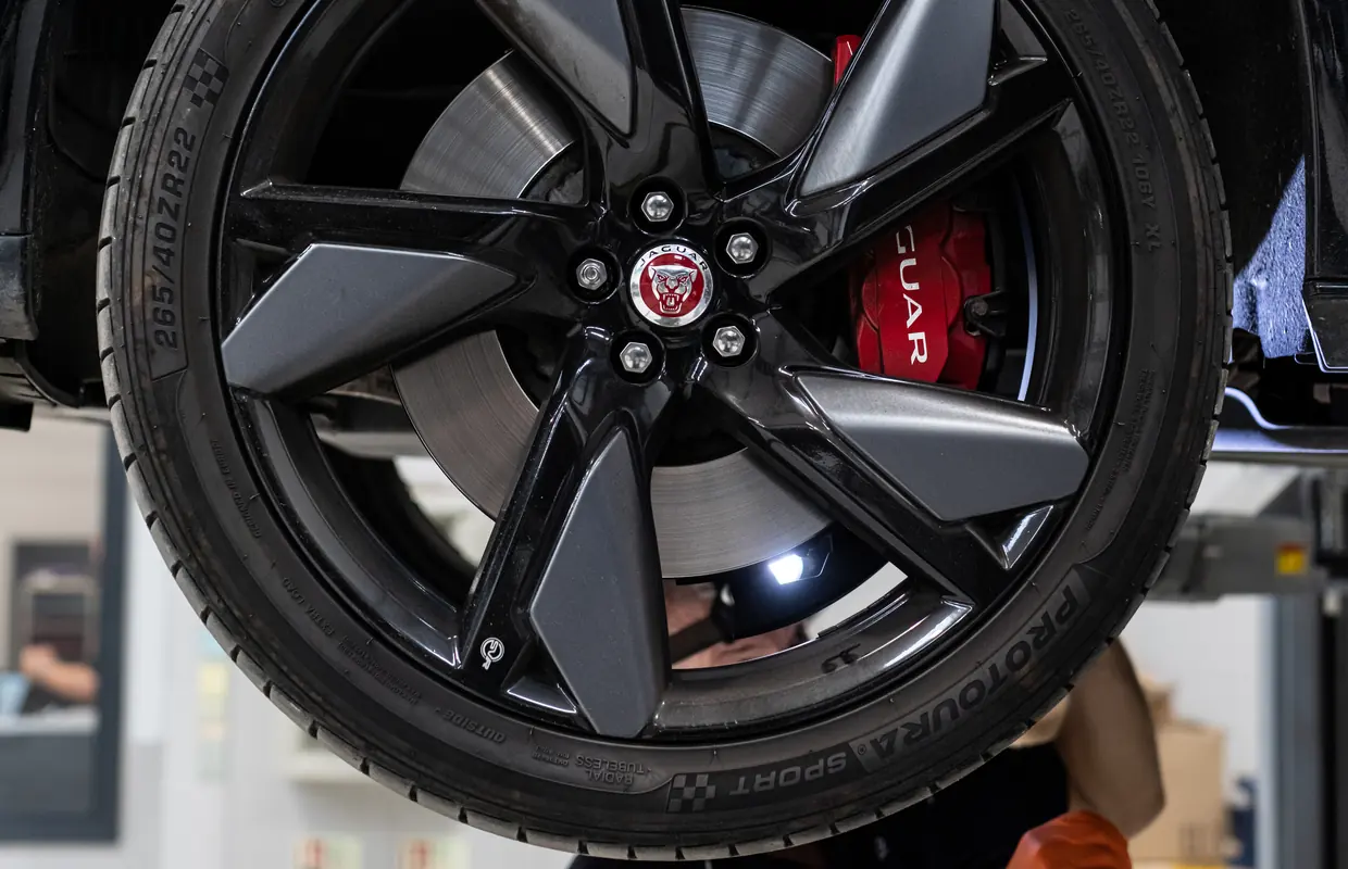 A gloss black Jaguar alloy wheel with a red brake caliper on a car raised on the lift