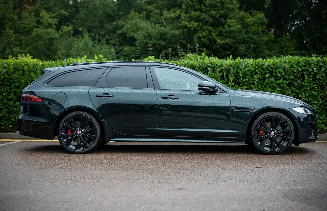 A freshly detailed British Racing Green Jaguar XF Sportbrake parked in front of a hedge