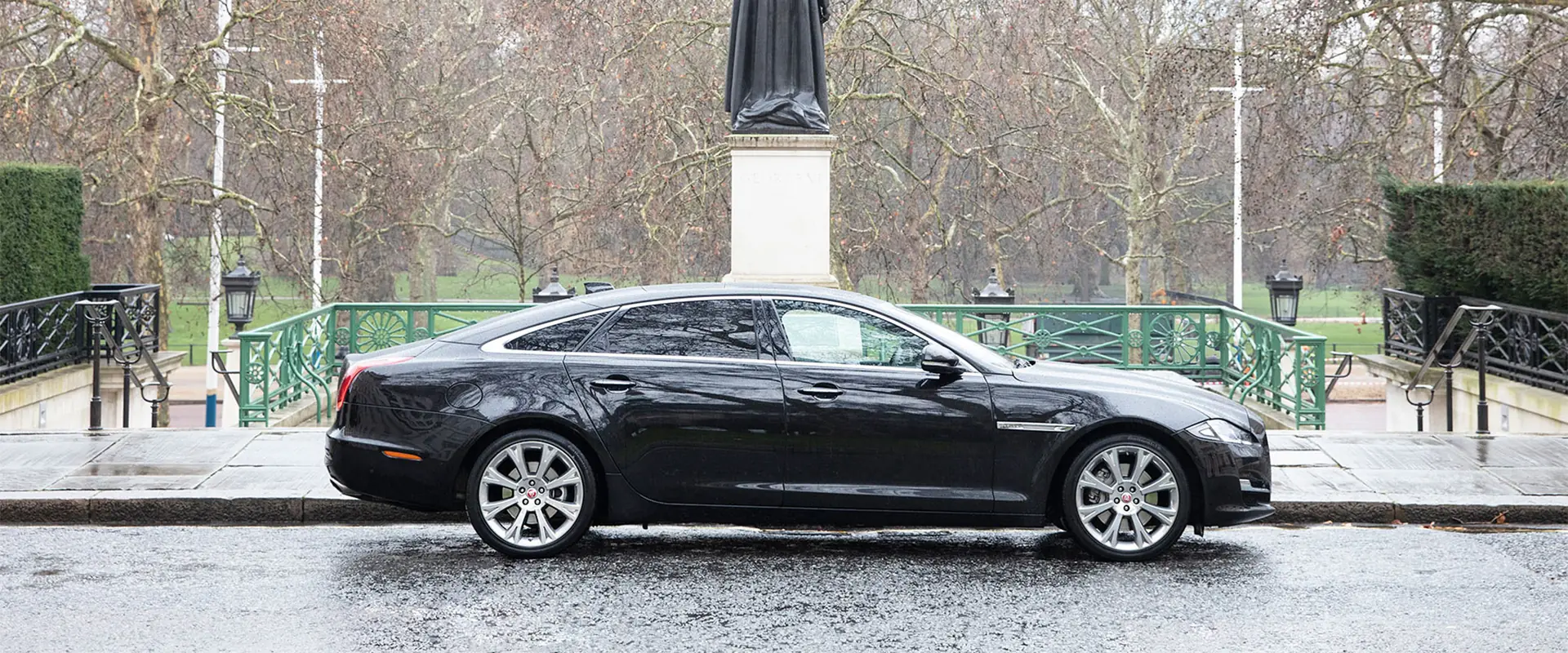 A black Jaguar XJ saloon parked beside a statue on a wet London street