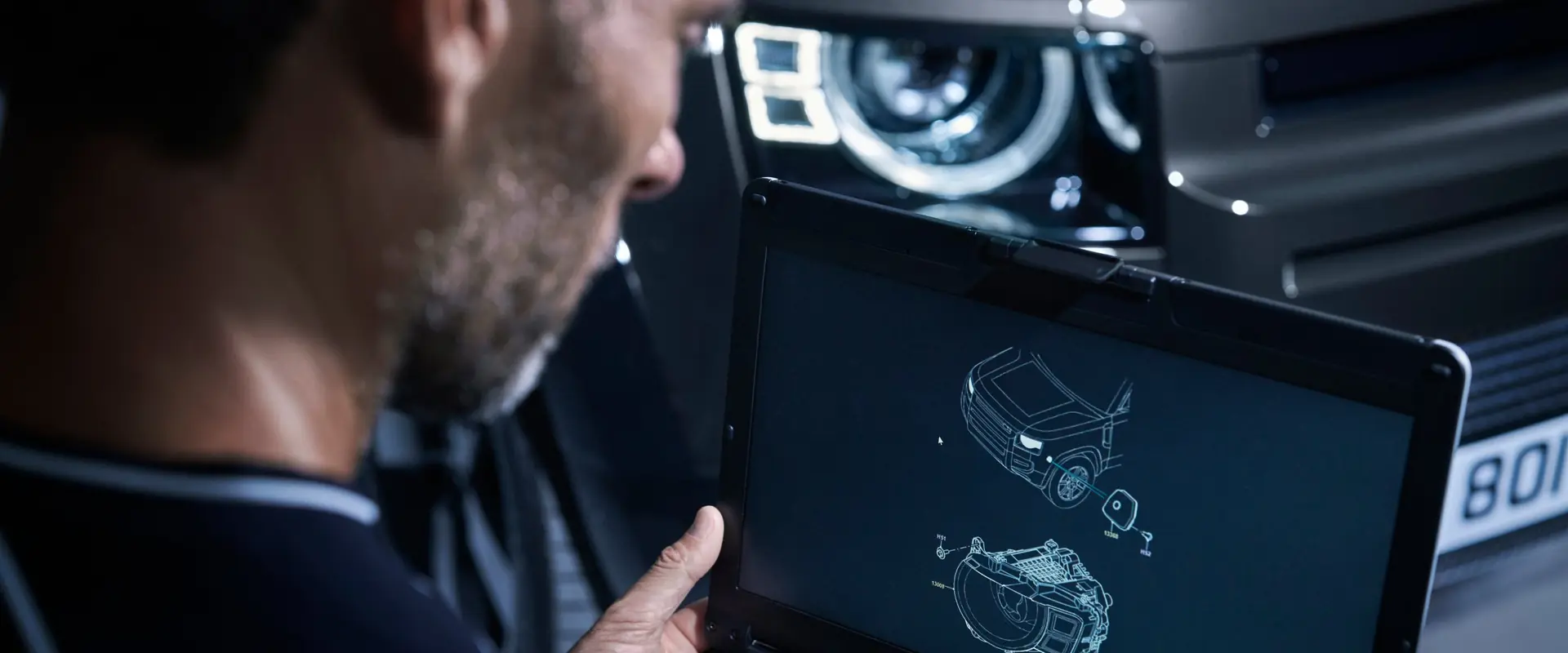 A JLC technician checking Jaguar Land Rover diagnostic data on a laptop in front of a Defender