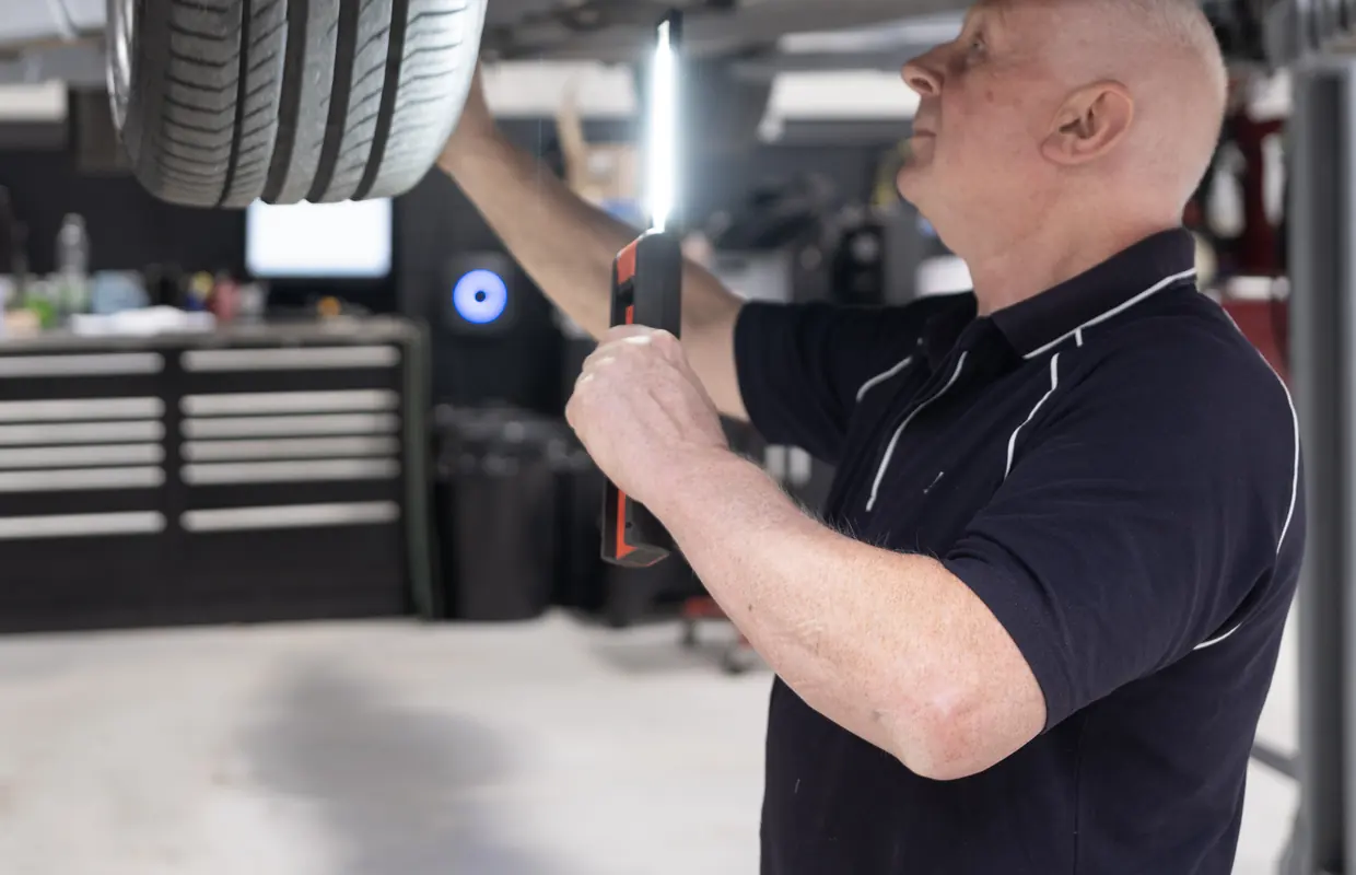A JLC technician inspecting a tyre and underside of a car on the lift with an inspection lamp